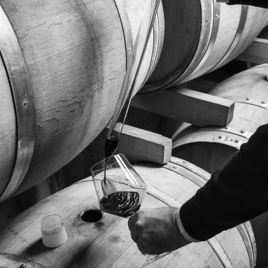Italy, Sicily, red wine pouring from a wooden barrel into a glass in a wine cellar